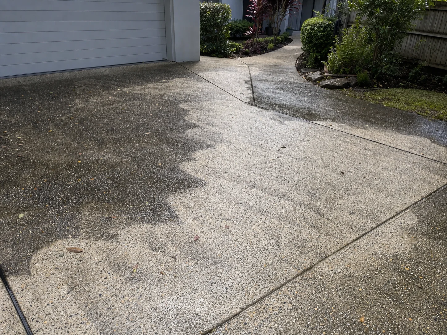 Rough half-cleaned Brisbane driveway project with irregular pressure washing passes and wet aggregate concrete